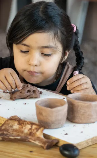 niña atacameña jufando con barro junto a artesanias tipicas de barro